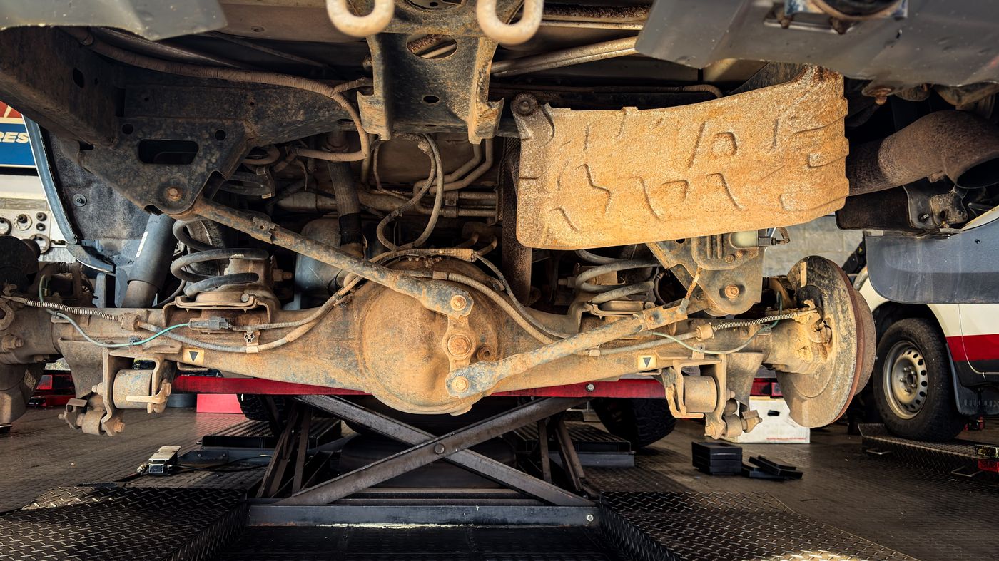 An axle and suspension under a raised vehicle showing orange-brown surface corrosion without the large rust holes in the final example